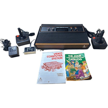 Vintage Atari video computer system with controllers, power cord, and manuals on a white background
