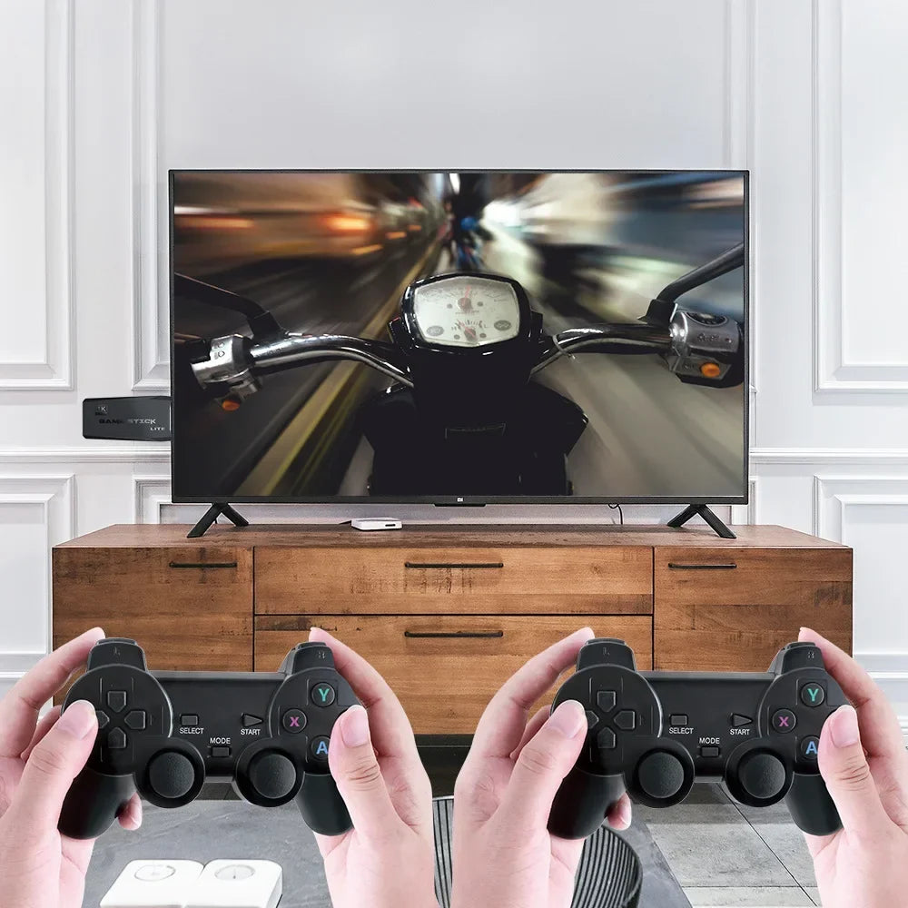 Two hands holding gaming controllers in front of a TV displaying a motorcycle game.