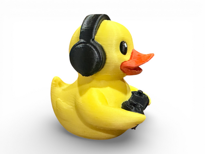 A yellow rubber duck wearing black headphones and holding a black object, shown on a clean white background.
