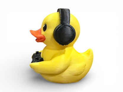A yellow rubber duck figurine wearing black headphones and holding a black controller, shown against a plain white background.