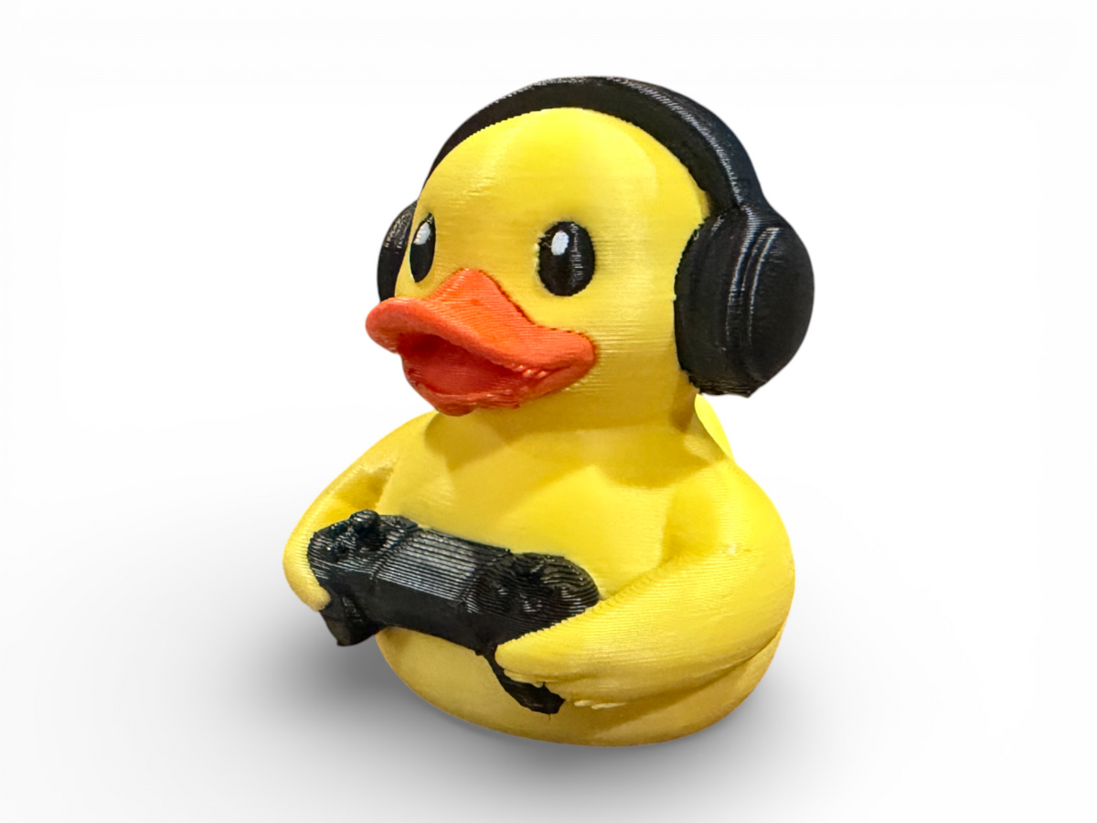 A yellow rubber duck toy wearing black headphones and holding a black game controller, shown on a clean white background.