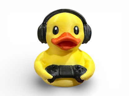 A yellow rubber duck toy wearing black headphones and holding a black game controller, shown against a plain white background.
