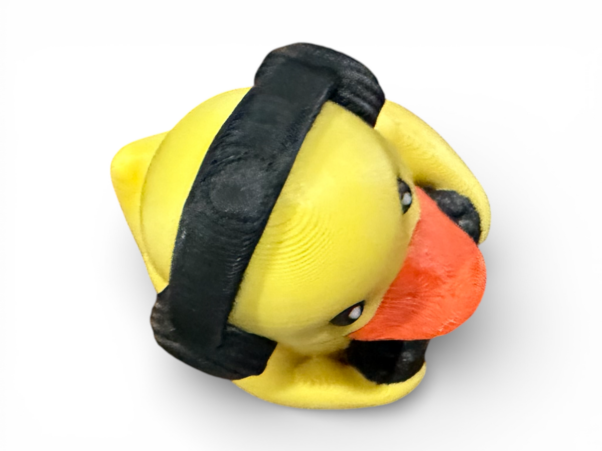A yellow duck-shaped object with a black strap-like band around it and a bright orange beak, photographed on a plain white background.