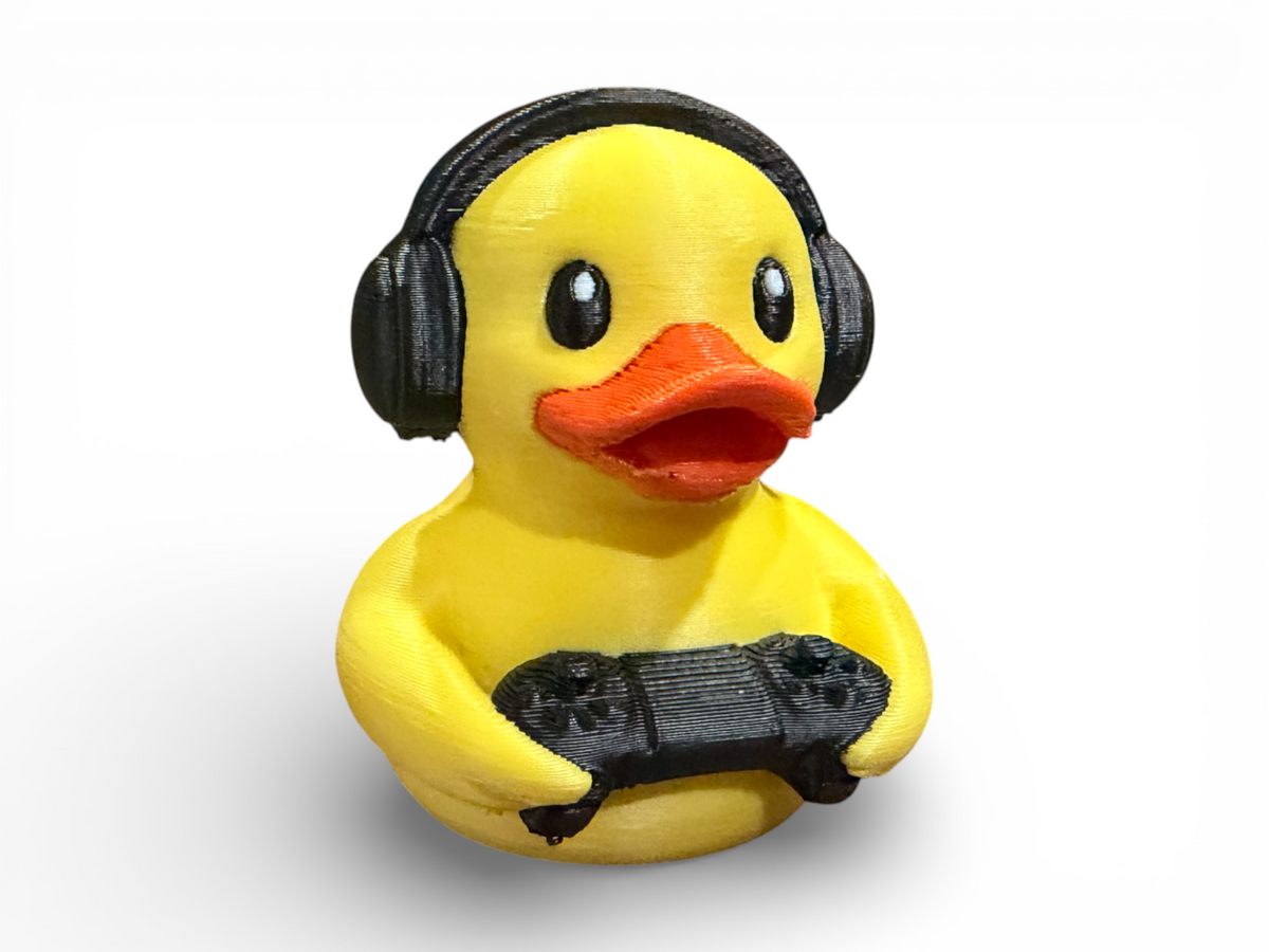 A yellow rubber duck toy wearing black headphones and holding a black game controller, shown against a plain white background.